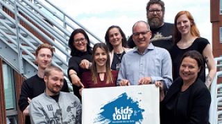 astendo-team haelt plakat mit logo kids-tour berlin in die Kamera
